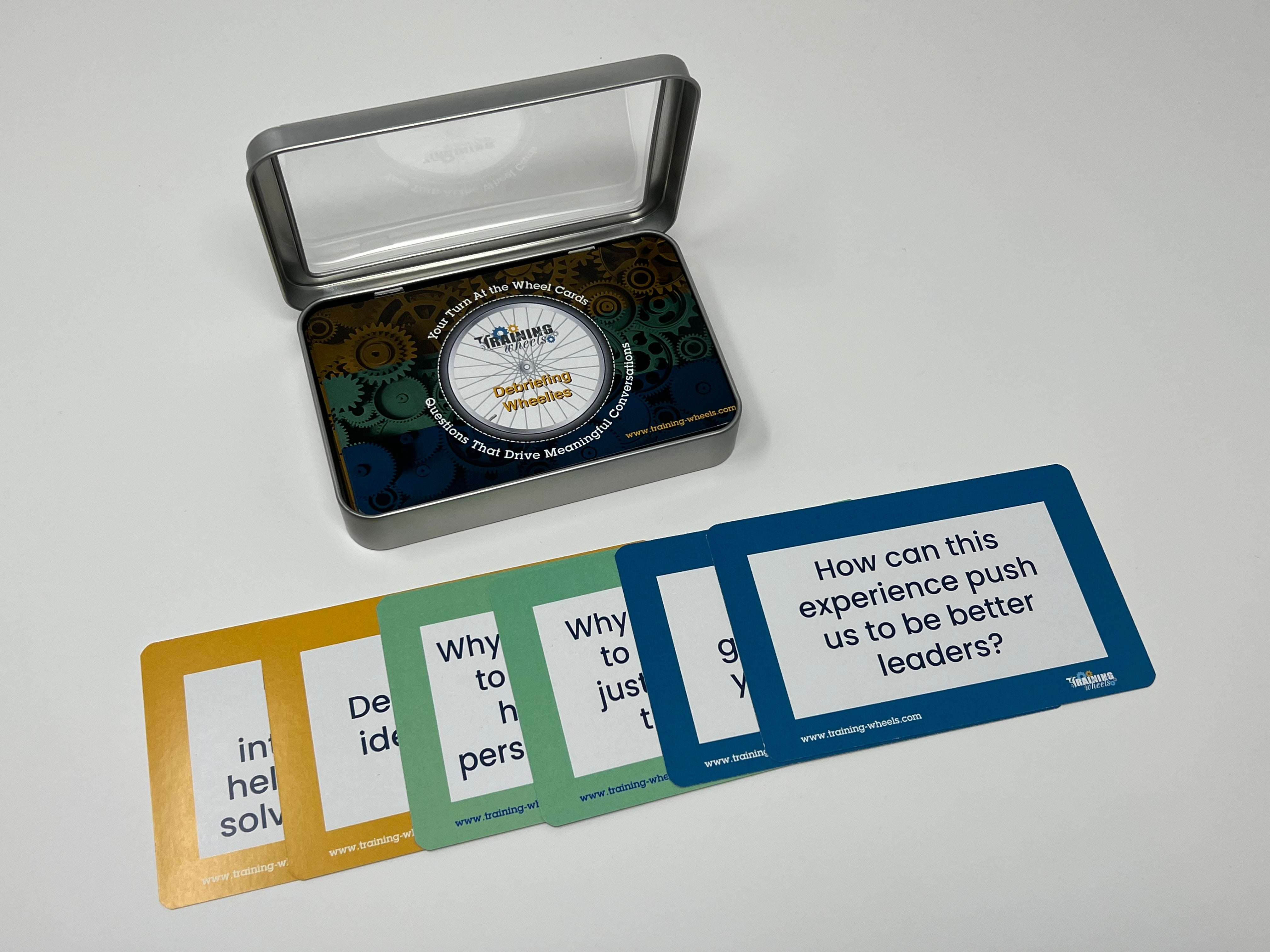 A set of color-coded debriefing question cards displayed outside of a plastic storage container, with a clear lid showing a thumball inside.