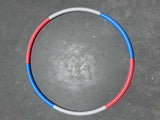 A sectional hula hoop with red and blue segments on a gray floor.