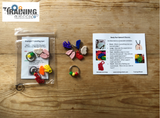 The image shows a Body Part Keychain which includes various charms shaped like body parts and stoplight beads, displayed on a wooden surface alongside its packaging.