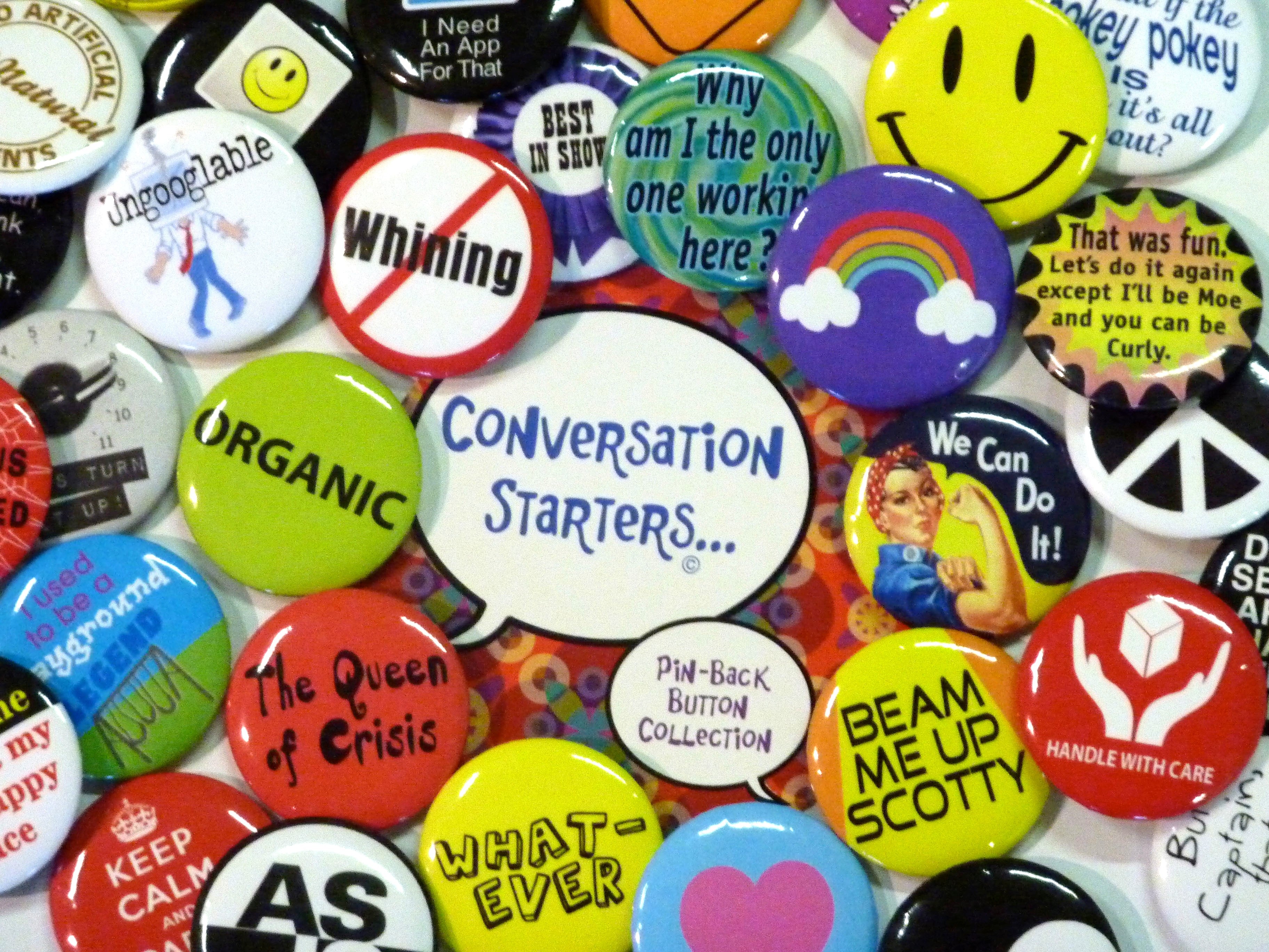 Assortment of colorful pin back buttons with various images and slogans, used as conversation starters and icebreakers for group activities.