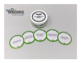 A set of round, green cards with spiritual icebreaker questions laid out in a row in front of a plastic container with a label.