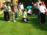 A group of participants collaboratively assembling a web structure from metal and rope components, focused on matching a black-and-white design pattern.