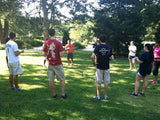 A group of people standing on grass, participating in an activity that involves maneuvering a small ball through an obstacle course using a bull ring.