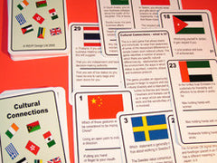 A collection of cards from the "Cultural Connections" card game displayed on a red surface, featuring flags and questions related to cultural diversity.