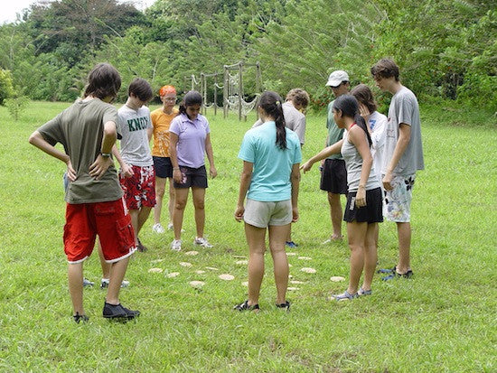 A group of people standing on numbered discs on a grassy field, participating in a team building activity.